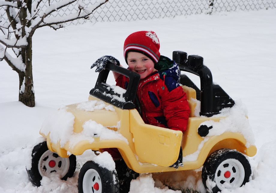 Little boy in toy car, driving in snow